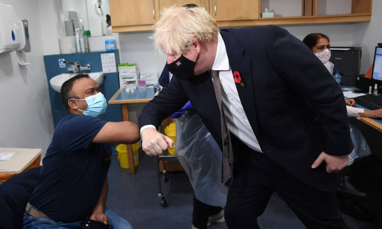 O primeiro-ministro da Grã-Bretanha, Boris Johnson, cumprimenta um homem recebendo uma vacina de reforço contra a covid durante uma visita a um centro de vacinação Foto: JEREMY SELWYN / AFP