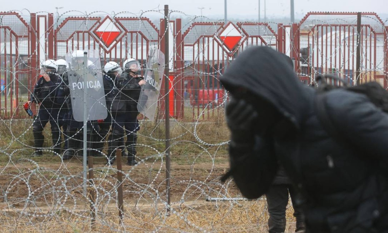 Policiais poloneses atiram bombas de gás contra migrantes que reage à fumaça na fronteira entre a Bielorrússia e a Polônia Foto: LEONID SHCHEGLOV / AFP