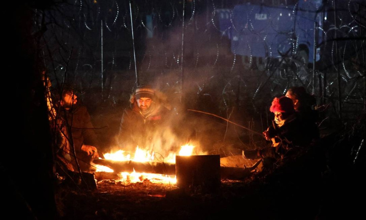 Migrantes com o objetivo de cruzar para a Polônia se aquecem em um incêndio na fronteira bielo-polonesa na região de Grodno Foto: MAXIM GUCHEK / AFP