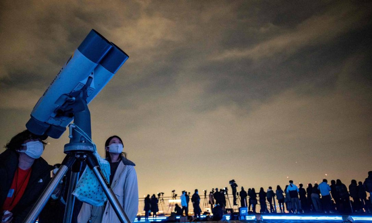 As pessoas observam o céu noturno com um telescópio enquanto fotógrafos e videojornalistas documentam um eclipse lunar do deck de observação de Roppongi Hills em Tóquio Foto: PHILIP FONG / AFP