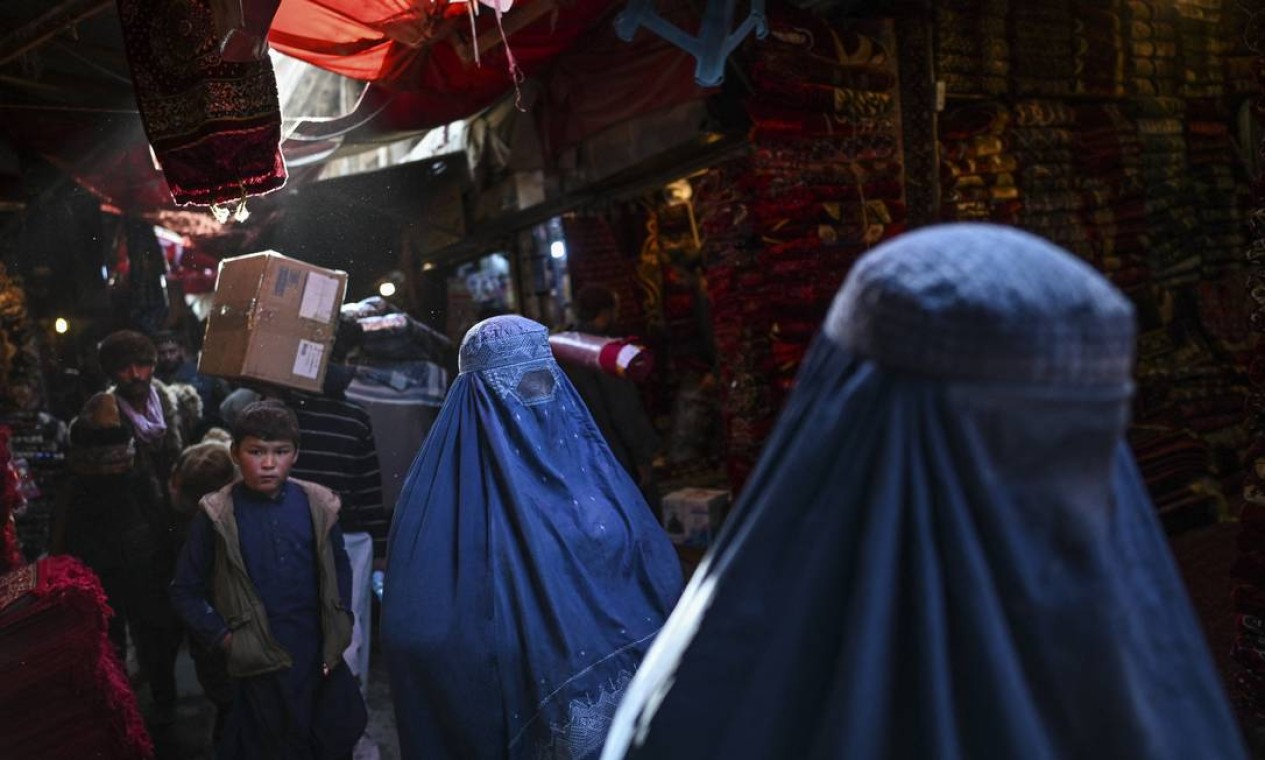Mulheres vestidas de burca caminham ao longo de um mercado de tapetes em Cabul Foto: HECTOR RETAMAL / AFP