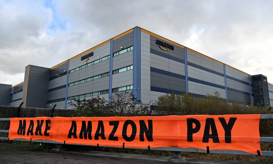 Ativistas exibem cartaz de protesto contra denúncias sobre manobras da gigante do varejo Amazon para não pagar devidos impostos onde atua, em Tilbury, a leste de Londres, na Inglaterra Foto: BEN STANSALL / AFP