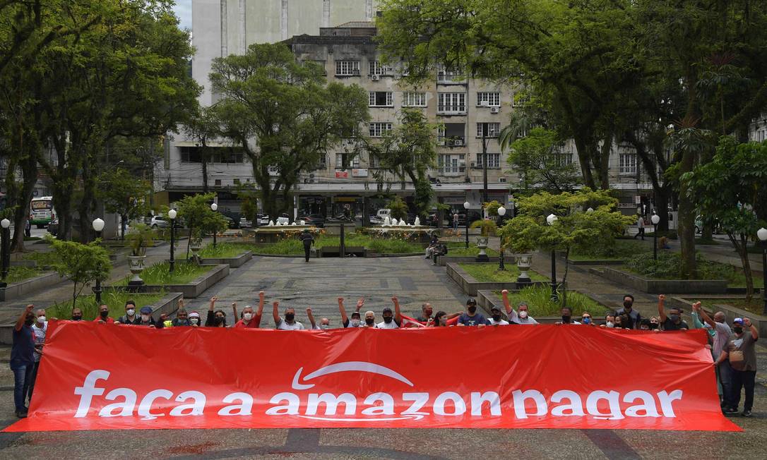 Trabalhadores do porto e membros de sindicatos se unem ao protesto global contra a gigante do comércio on-line levando uma faixa onde se lê Faça a Amazon pagar ('Make Amazon Pay', em inglês), no centro da cidade de Santos Foto: Nelson Almeida / AFP