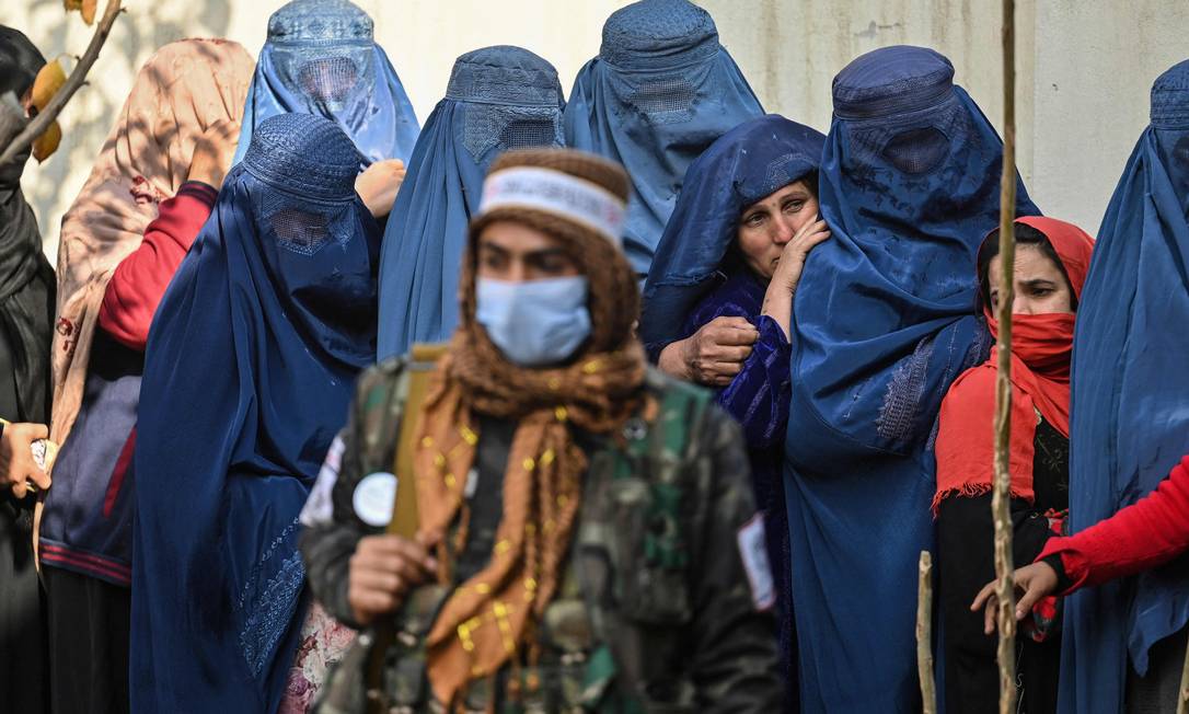 Guerrilheiro do Talebã fica de guarda enquanto as mulheres esperam em uma fila durante a distribuição de dinheiro do Programa Mundial de Alimentos em Cabul, Afeganistão Foto: HECTOR RETAMAL / AFP