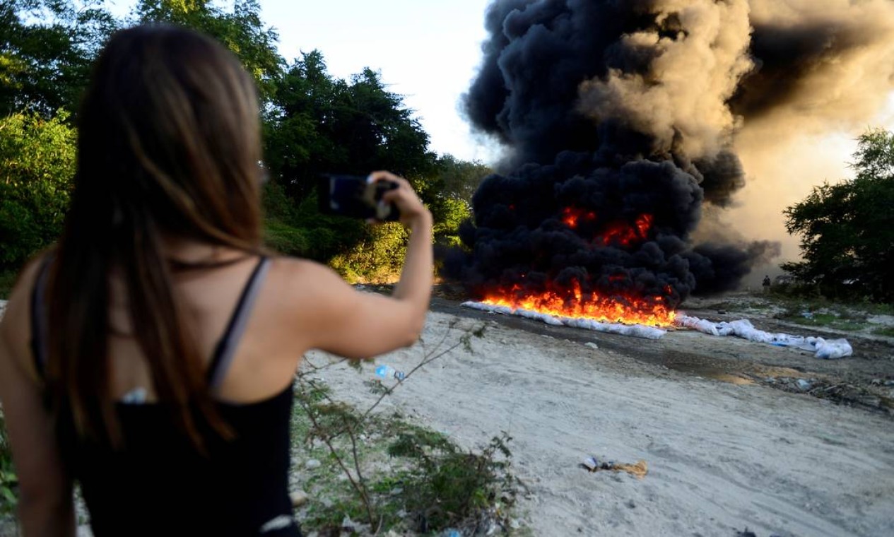 Mulher filma com seu telefone a incineração de pacotes de cocaína, parte de uma apreensão de drogas em alto mar de 135 pacotes pela Força Naval de El Salvador, em uma base policial em Ilopango Foto: JESSICA ORELLANA / REUTERS