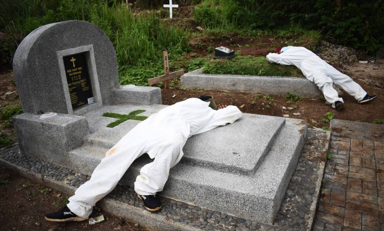 JUNHO - Coveiros, usando EPI descansam sobre túmulos em Bandung, Indonésia. Ainda no segundo ano da pandemia, já com vacina para a Covid-19, coveiros foram sobrecarregados pela letalidade da pandemia Foto: TIMUR MATAHARI / AFP