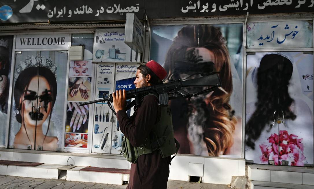 Soldado talibã passa por um salão de beleza com imagens de mulheres pichadas com tinta em Cabul, no Afeganistão Foto: WAKIL KOHSAR / AFP