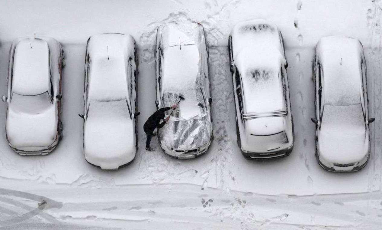 Homem varre a neve que cobre um carro em Moscou Foto: NATALIA KOLESNIKOVA / AFP