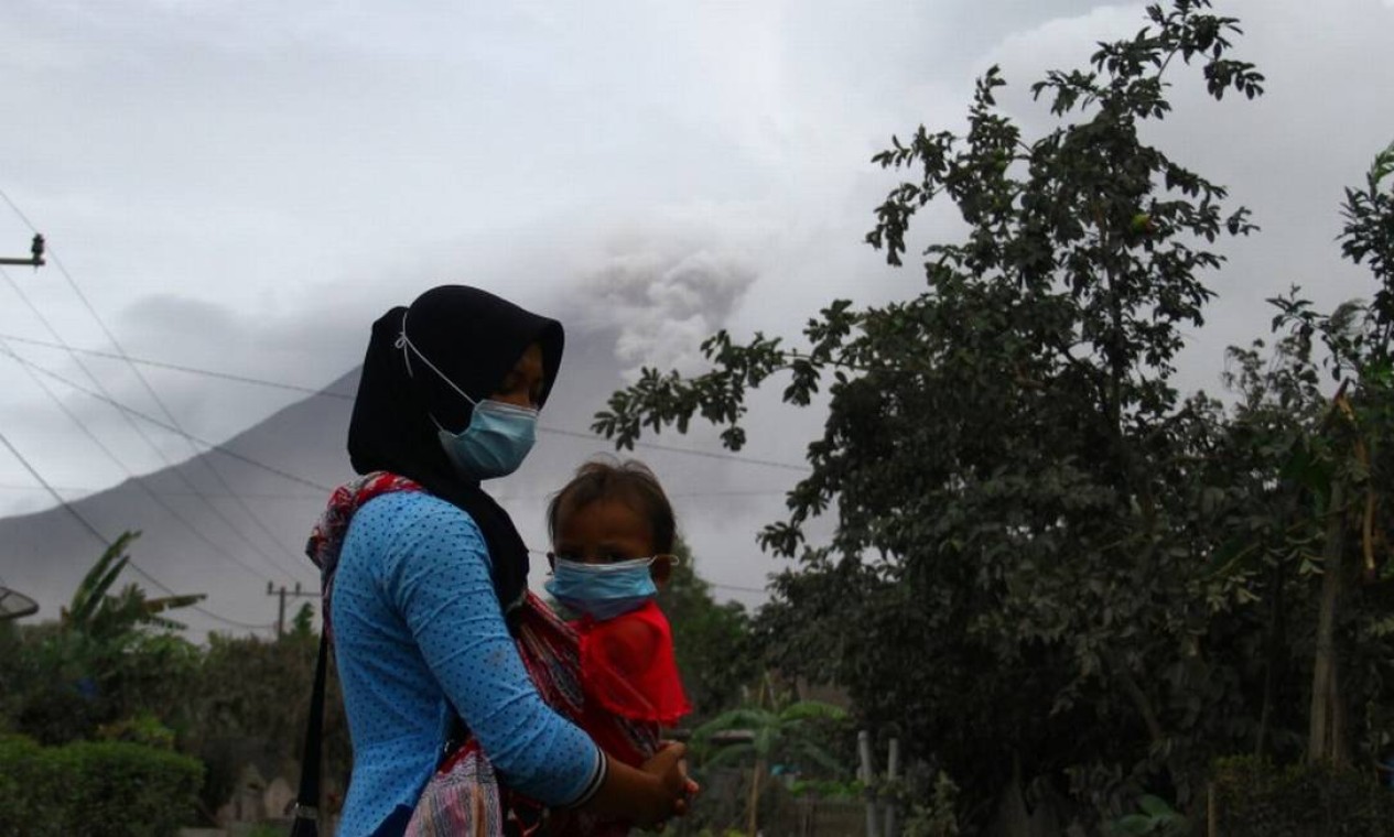 Mulher carrega seu filho usando máscaras faciais de proteção contra cinzas vulcânicas em Supiturang Foto: ANTARA FOTO / via REUTERS