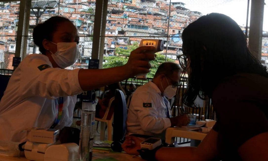 Profissional de saúde verifica a temperatura de paciente com suspeita de gripe em polo municipal do Alemão Foto: Fabiano Rocha / Agência O Globo