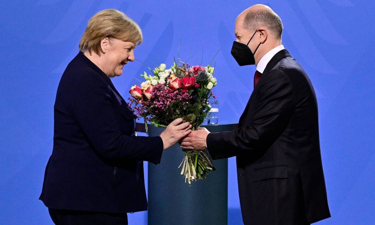 O chanceler alemão, Olaf Scholz, presenteia com buquê de flores sua antecessora, Angela Merkel, durante a cerimônia de transferência do cargo, em Berlim Foto: JOHN MACDOUGALL / AFP