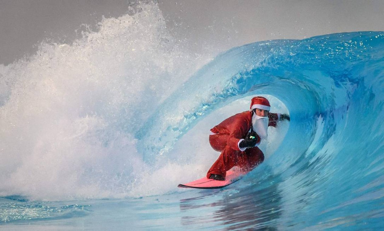 Surfista vestido de Papai Noel surfa uma onda artificial em água fria de 0,6 grau, na piscina de ondas da Baía de Alaia cercada pelos Alpes suíços, em Sion Foto: FABRICE COFFRINI / AFP
