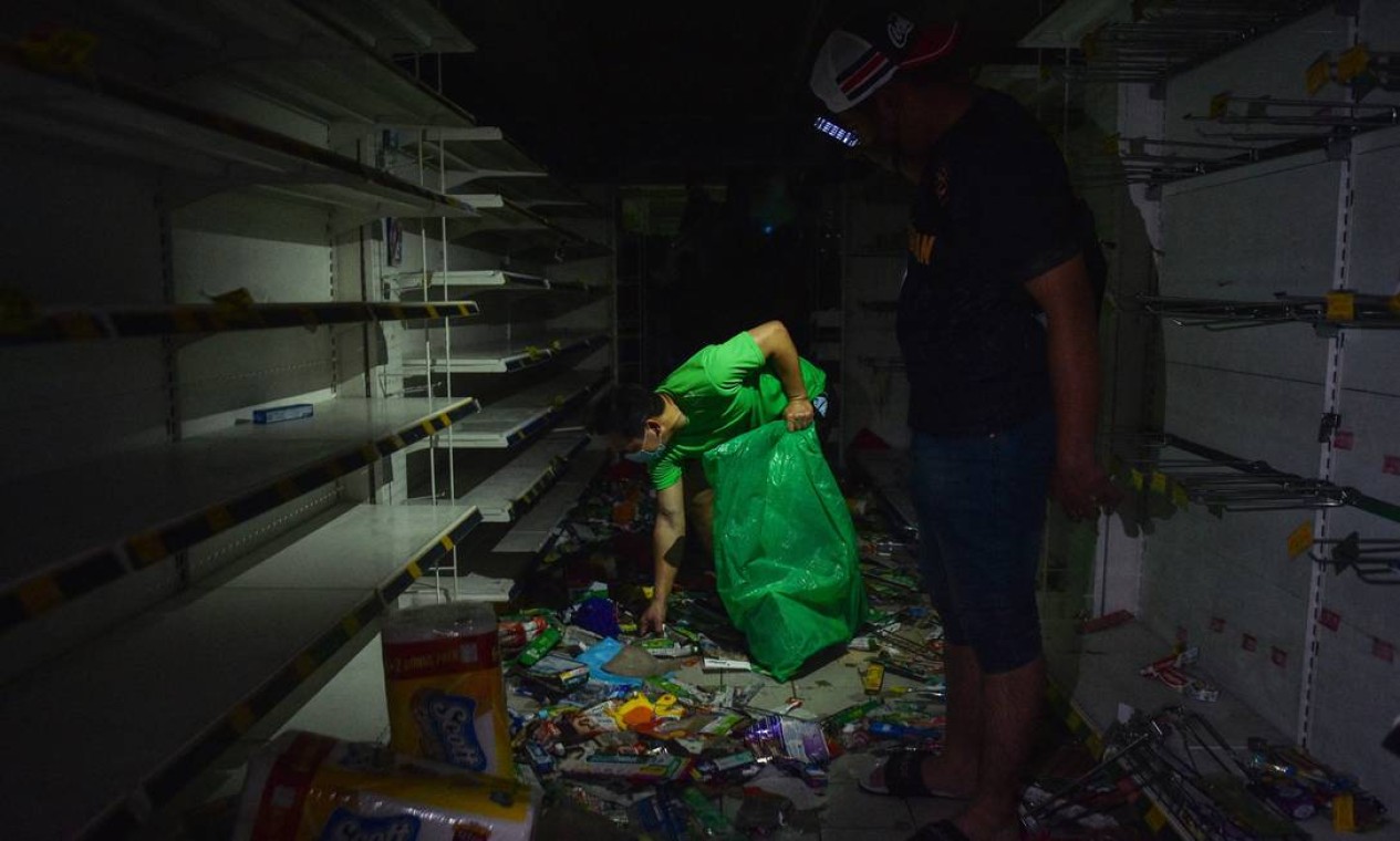 Homem usa celular como lanterna enquanto outro procura por itens em um supermercado danificado em Shah Alam, Selangor. A Malásia enfrenta grandes inundações que deixaram pelo menos 14 mortos e mais de 70.000 desabrigados Foto: ARIF KARTONO / AFP