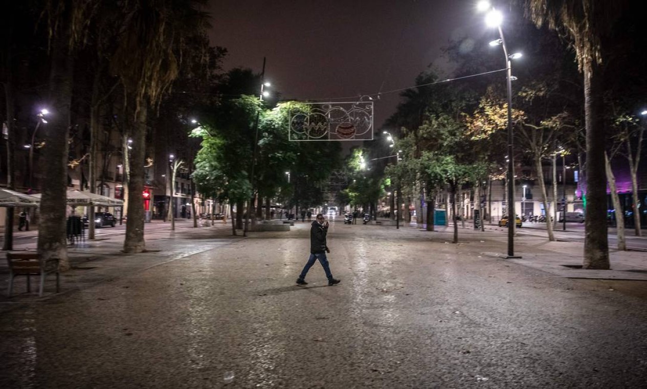 Pedestre caminha na vazia rua central de La Rambla, em Barcelona, na noite de 23 de dezembro para 24. A Catalunha espanhola impôs toque de recolher noturno, fechou boates e limitou reuniões sociais para combater um aumento recorde em infecções por Covid-19 Foto: ANGEL GARCIA / AFP