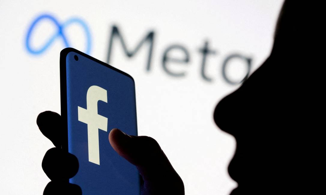 Mulher segura celular com logo do Facebook em frente a uma tela exibindo a logo da Meta, o novo nome do Facebook Foto: Dado Ruvic / Reuters