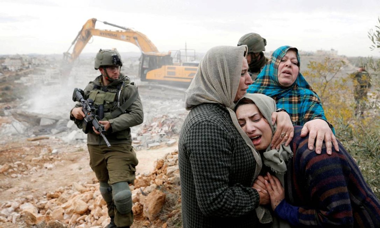 Mulher palestina é consolada enquanto uma máquina israelense demole sua casa em construção, em Hebron, na Cisjordânia ocupada por israelenses Foto: MUSSA ISSA QAWASMA / REUTERS