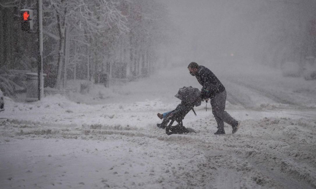 Homem tenta atravessar com carrinho de bebê uma rua durante tempestade de neve no centro de Washington Foto: ROBERTO SCHMIDT / AFP