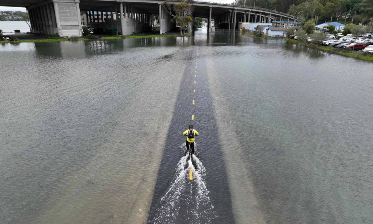 Homem anda de bicicleta ao longo de um trecho da ciclovia de Sausalito inundada em Mill Valley, Califórnia Foto: JOSH EDELSON / AFP