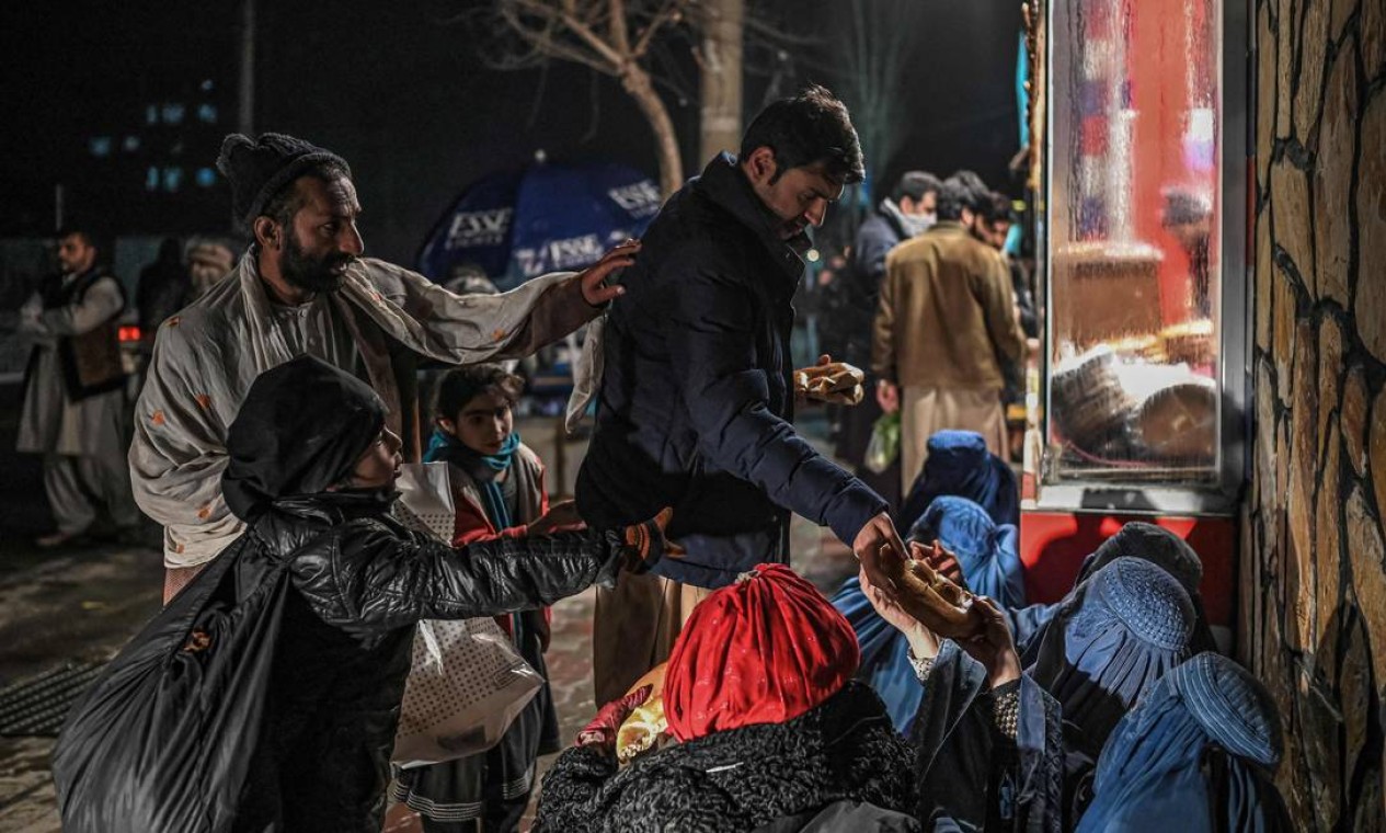 Homem distribui comida para mulheres afegãs vestidas de burca em frente a uma padaria de Cabul Foto: MOHD RASFAN / AFP