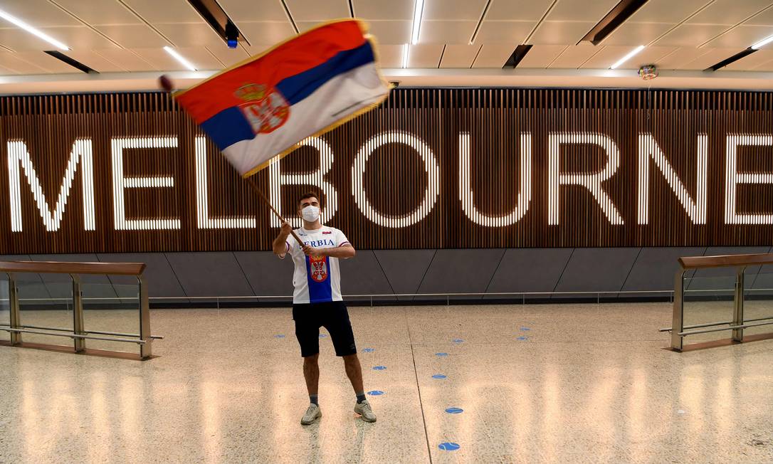 Um fã de Novak Djokovic balança uma bandeira da Sérvia no Aeroporto Internacional de Melbourne, na Austrália, onde o tenista foi barrado por não comprovar vacinação contra Covid Foto: WILLIAM WEST / AFP