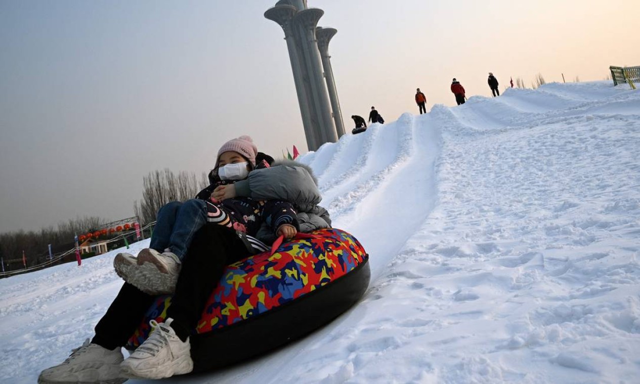 Pessoas escorregam em uma colina coberta de neve perto do Parque Olímpico de Pequim, sede dos Jogos Olímpicos de Inverno de 2022 Foto: NOEL CELIS / AFP