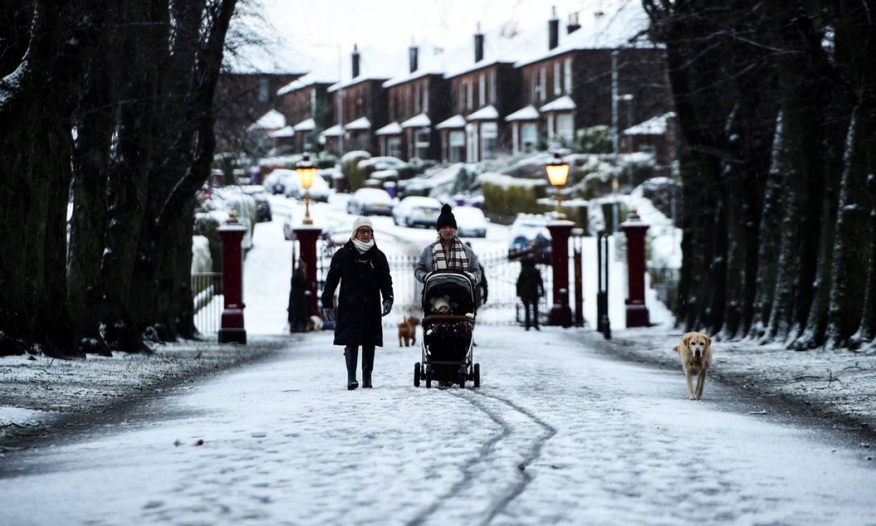 Pessoas caminham com um cachorro na neve em Victoria Park, no extremo oeste de Glasgow, no Reino Unido Foto: ANDY BUCHANAN / AFP