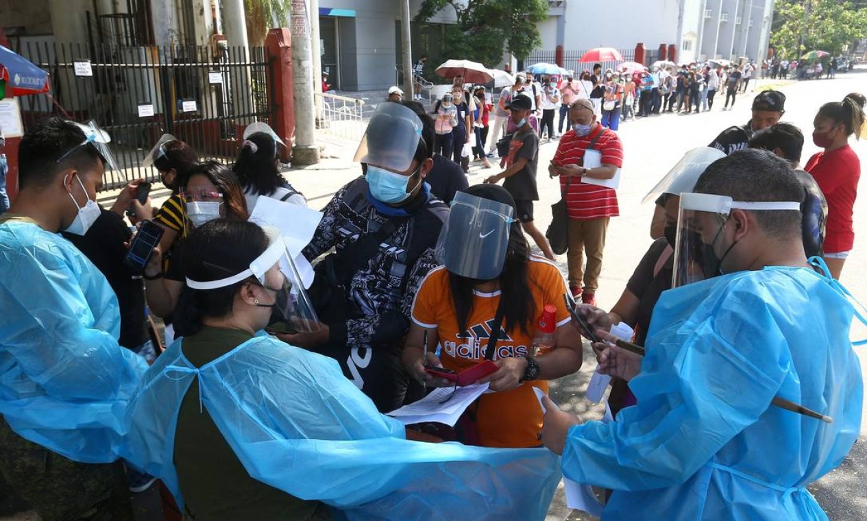 Profissionais de saúde verificam documentos de pessoas em fila para os testes de Covid em um ginásio de Manila à medida que crescem os casos de infecção na capital do país Foto: AFP