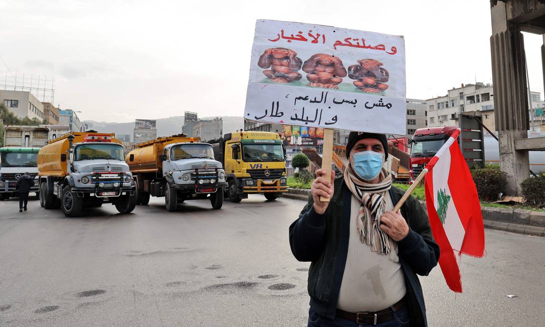 Manifestante libanês segura um cartaz enquanto caminhões-tanque bloqueiam uma estrada na capital do Líbano, Beirute, durante uma greve geral de transportes públicos e sindicatos de trabalhadores Foto: ANWAR AMRO / AFP
