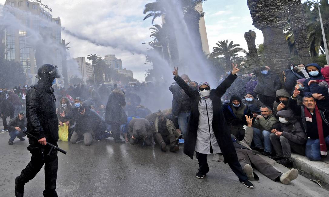 Manifestante na Tunísia faz o sinal de "V" com as mãos, em referência a vitória, enquanto forças de segurança utilizam canhões de água para dispersar protesto antigoverno Foto: FETHI BELAID / AFP