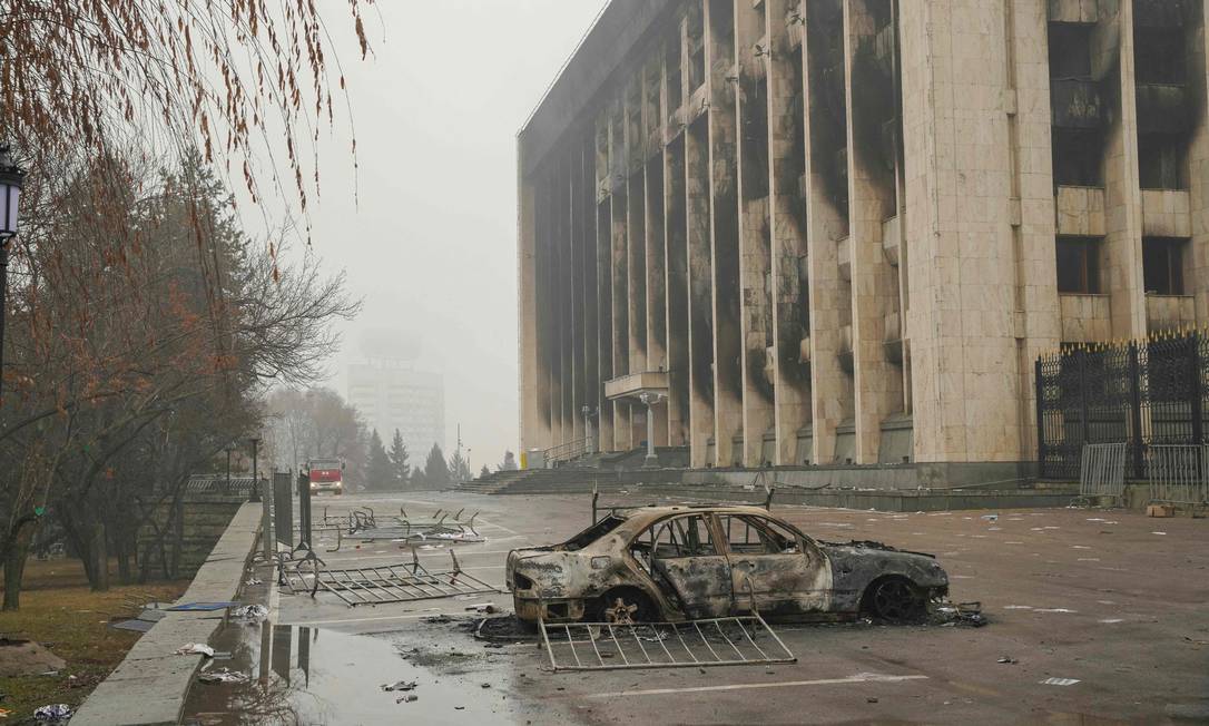 Veículo destruído em frente a um prédio administrativo queimado no centro de Almaty, a capital financeira e principal cidade do Cazaquistão que foi o principal palco dos protestos no país Foto: ALEXANDR BOGDANOV / AFP / 7-1-2022
