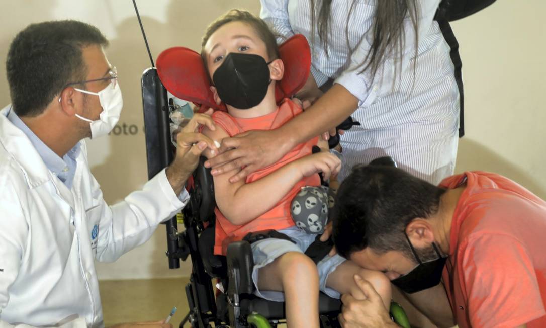 O menino Davi é vacinado ao lado do pai, Paulo Silva, que se emociona e chora Foto: Gabriel de Paiva / Agência O Globo