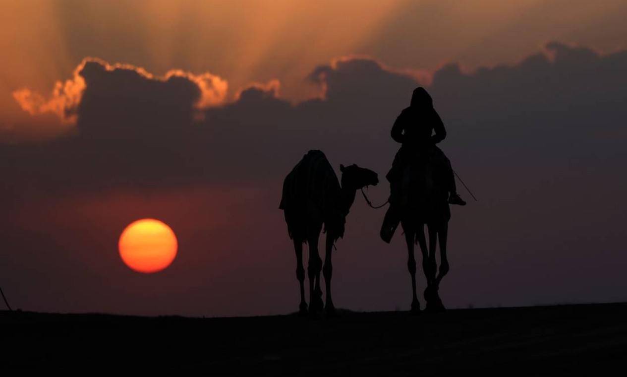 Homens com seus camelos assistem ao nascer do sol durante o Mazayin Dhafra Camel Festival, no deserto perto da cidade de Madinat Zayed, cerca de 150 km a oeste da capital dos Emirados, Abu Dhabi Foto: KARIM SAHIB / AFP
