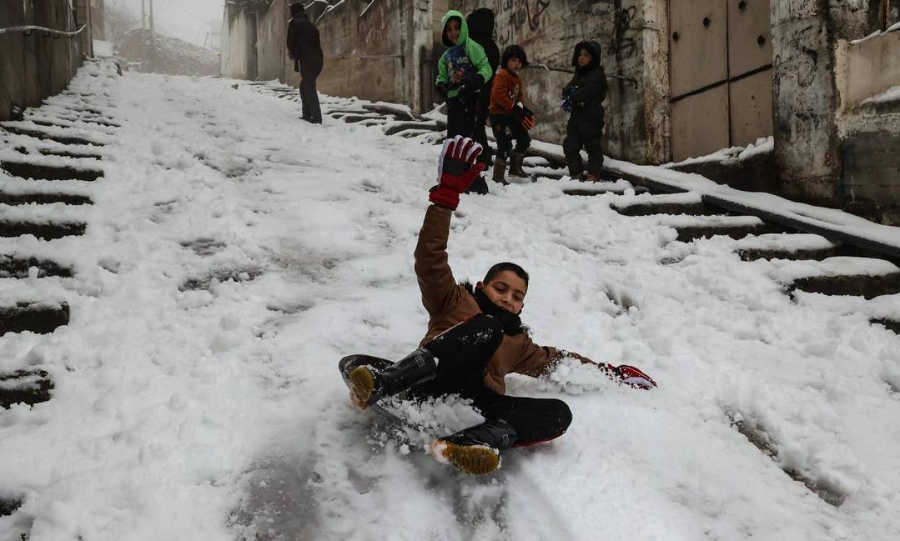 Crianças palestinas brincam em rua após uma queda de neve durante a noite na cidade ocupada de Hebron, na Cisjordânia Foto: HAZEM BADER / AFP
