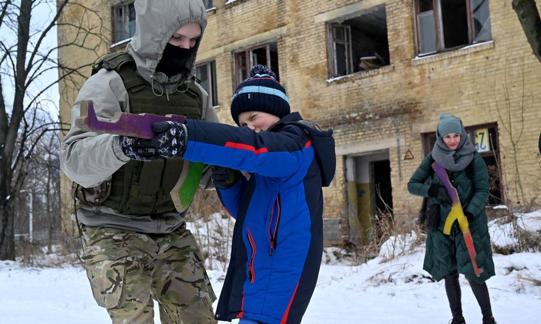 Um instrutor militar ensina civis segurando réplicas de madeira de fuzis Kalashnikov, enquanto eles participam de uma sessão de treinamento em uma fábrica abandonada na capital ucraniana de Kiev Foto: SERGEI SUPINSKY / AFP