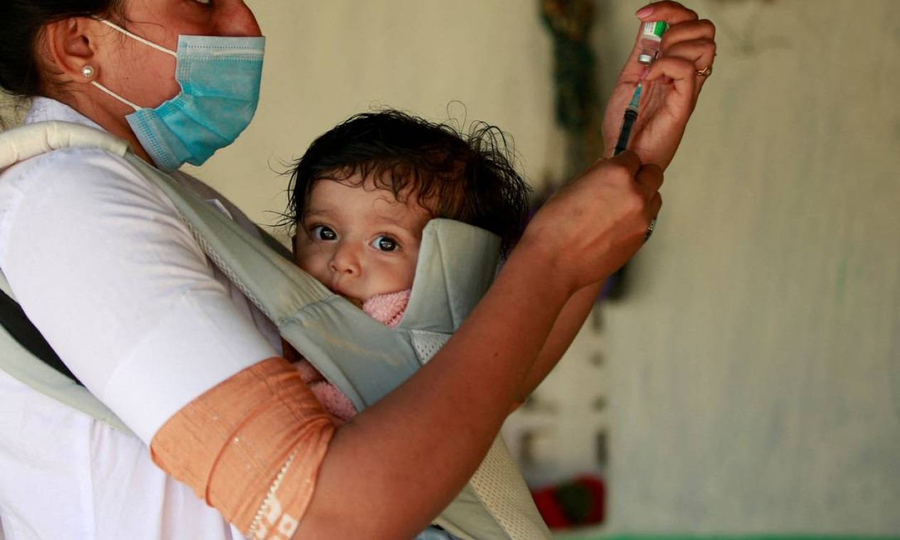 Asmita Koladiya, 29, uma profissional de saúde, carregando sua filha de oito meses, Jiyanshi Gaurang, se prepara para aplicar uma dose de vacina contra COVID-1 a um morador do distrito de Rajkot, no estado ocidental de Gujarat, Índia Foto: AMIT DAVE / REUTERS