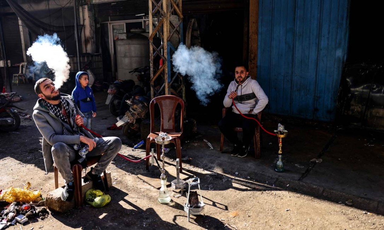 Homens libaneses fumam narguilé enquanto descansam do lado de fora de sua oficina em um beco do bairro pobre de Bab al-Tabbaneh, no norte de Trípoli, a cidade mais pobre do Líbano, onde dezenas de jovens teriam sido recrutados pelo grupo Estado Islâmico (EI) dezenas de jovens Foto: JOSEPH EID / AFP