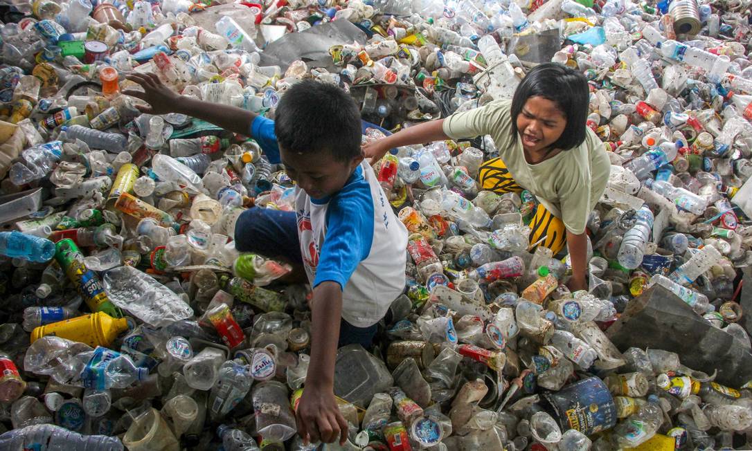 Crianças brincam em pilhas de resíduos plásticos coletados para reciclagem em Makassar, Indonésia Foto: ANDRI SAPUTRA / AFP