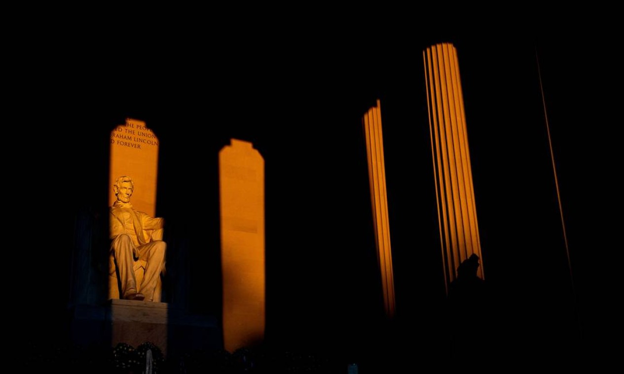 A estátua de Abraham Lincoln é iluminada ao nascer do sol enquanto um visitante caminha pelo Lincoln Memorial no Presidents Day em Washington, DC, Foto: STEFANI REYNOLDS / AFP
