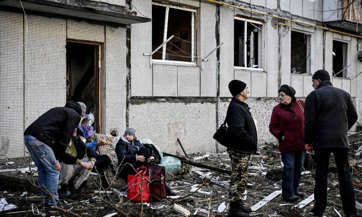 Civis ficam do lado de fora de um prédio destruído após bombardeios na cidade de Chuguiv. Foto: ARIS MESSINIS / AFP