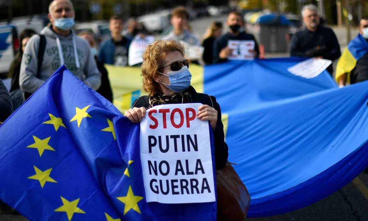 Manifestantes seguram cartazes com os dizeres "Pare Putin, não à guerra" e bandeiras da União Europeia e da Ucrânia durante um protesto contra a operação militar da Rússia na Ucrânia, em frente ao consulado russo em Barcelona, Espanha Foto: PAU BARRENA / AFP