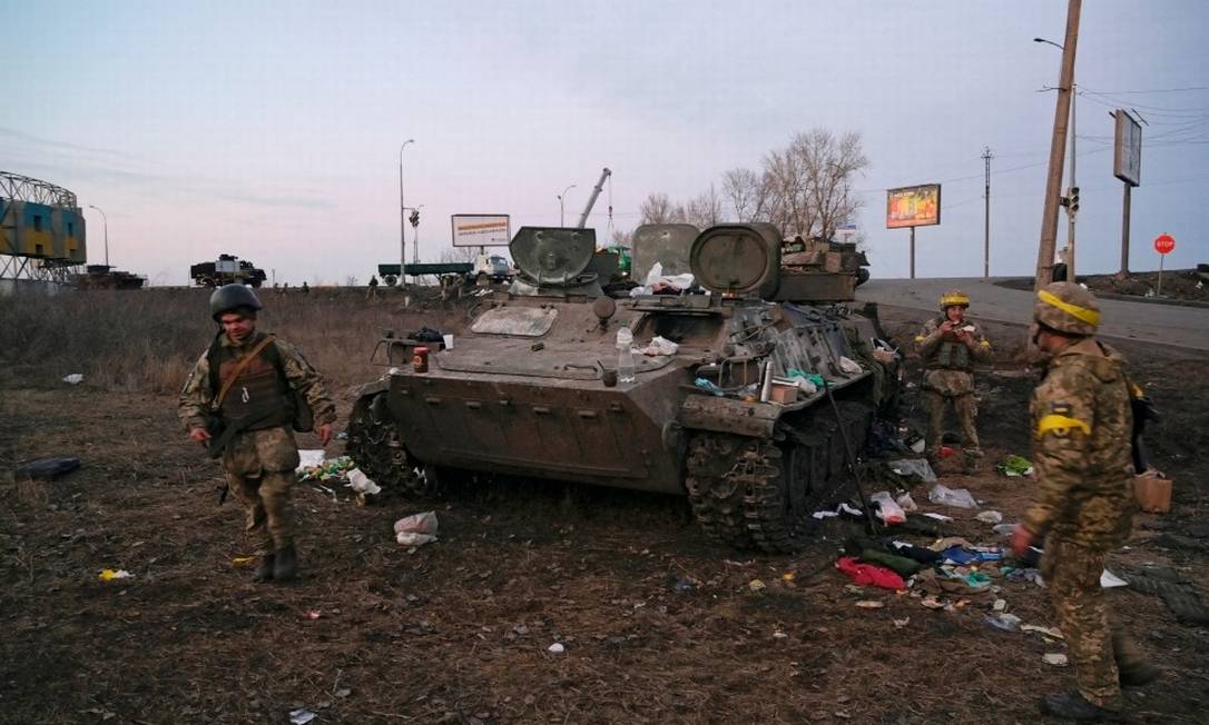 Militares ucranianos ao lado de um veículo blindado destruído, que eles dizem pertencer ao exército russo, nos arredores de Kharkiv Foto: MAKSIM LEVIN / REUTERS