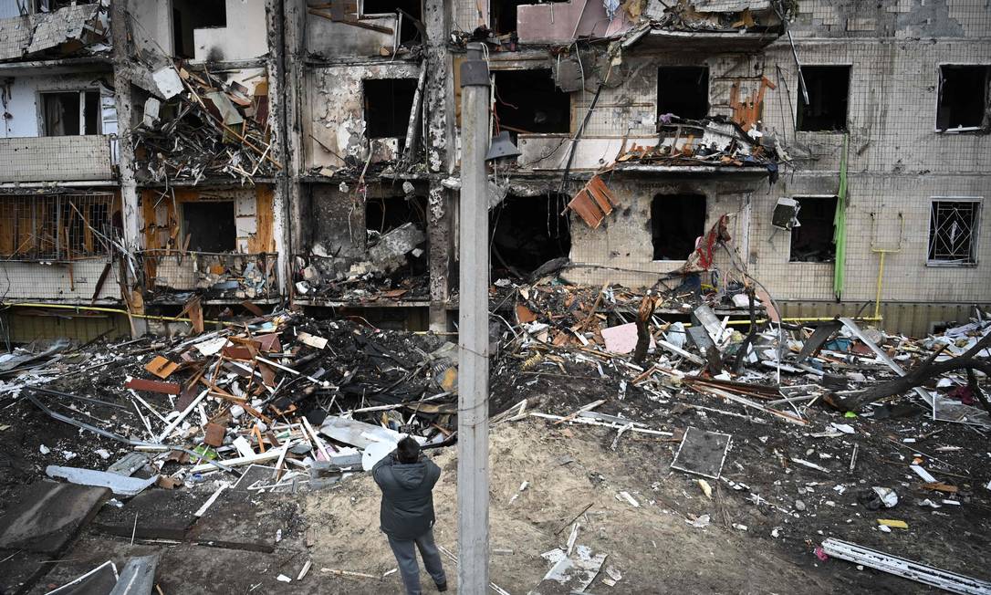 Homem tira fotos de um prédio residencial danificado na rua Koshytsa, um subúrbio da capital ucraniana Kiev Foto: DANIEL LEAL / AFP