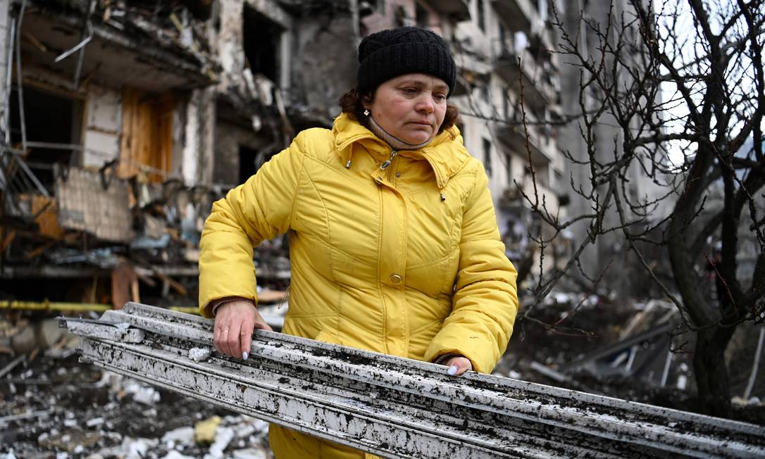 Uma mulher limpa destroços em um prédio residencial danificado na rua Koshytsa, um subúrbio da capital ucraniana Kiev Foto: DANIEL LEAL / AFP