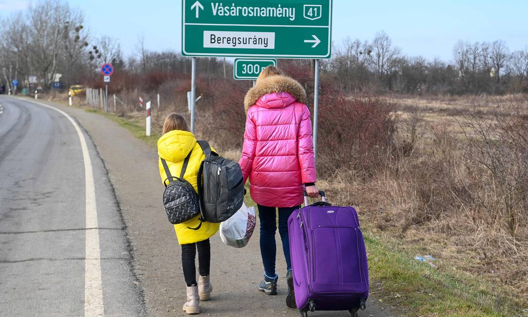 Uma mãe ucraniana caminha com sua filha ao longo da estrada da fronteira húngara-ucraniana perto de Beregsurany, Hungria, a cerca de 300 km da capital húngara Foto: ATTILA KISBENEDEK / AFP