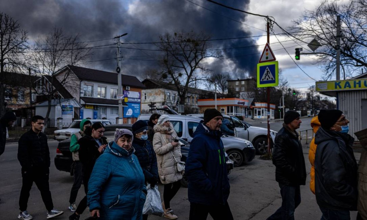 Pessoas fazem fila em frente a um supermercado enquanto fumaça sobe sobre a cidade de Vasylkiv, nos arredores de Kiev, após ataques russos noturnos atingirem um depósito de petróleo Foto: DIMITAR DILKOFF / AFP - 27/02/2022