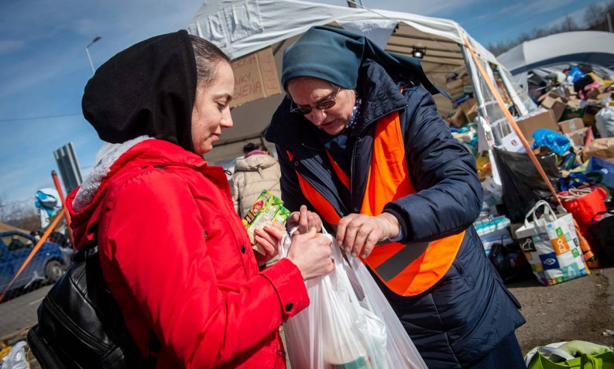 Voluntário eslovaco dá comida a um refugiado ucraniano na fronteira eslovaco-ucraniana em Vysne Nemecke, Eslováquia Foto: PETER LAZAR / AFP