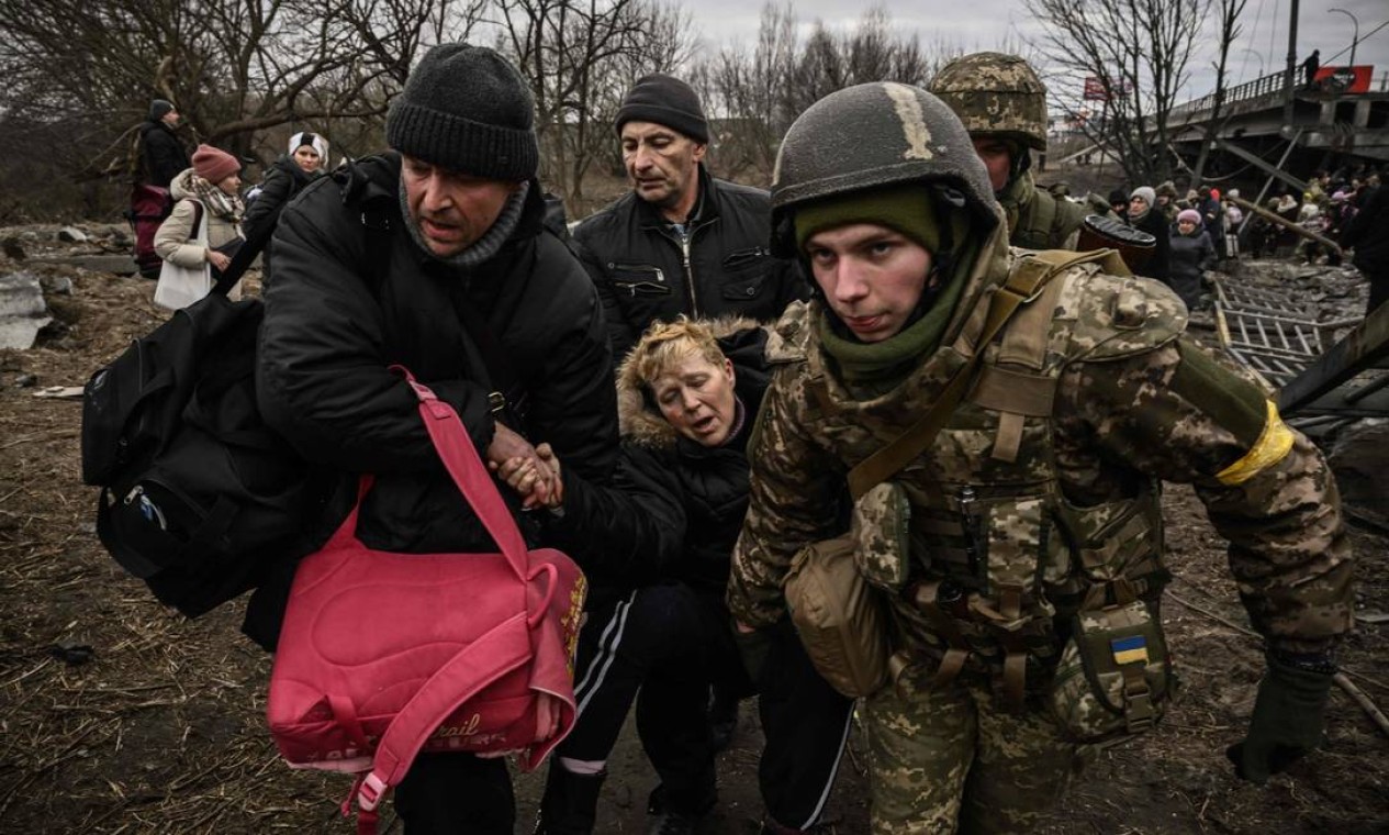 Mulher é assistida por soldados ucranianos enquanto pessoas evacuam a cidade de Irpin, a noroeste de Kiev, durante bombardeios pesados Foto: ARIS MESSINIS / AFP