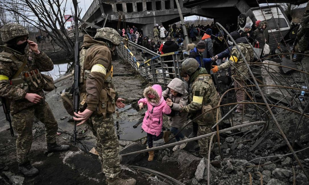 Pessoas atravessam uma ponte destruída ao evacuar a cidade de Irpin, a noroeste de Kiev, durante pesados bombardeios, 10 dias após a Rússia lançar um exército em invasão à Ucrânia Foto: ARIS MESSINIS / AFP