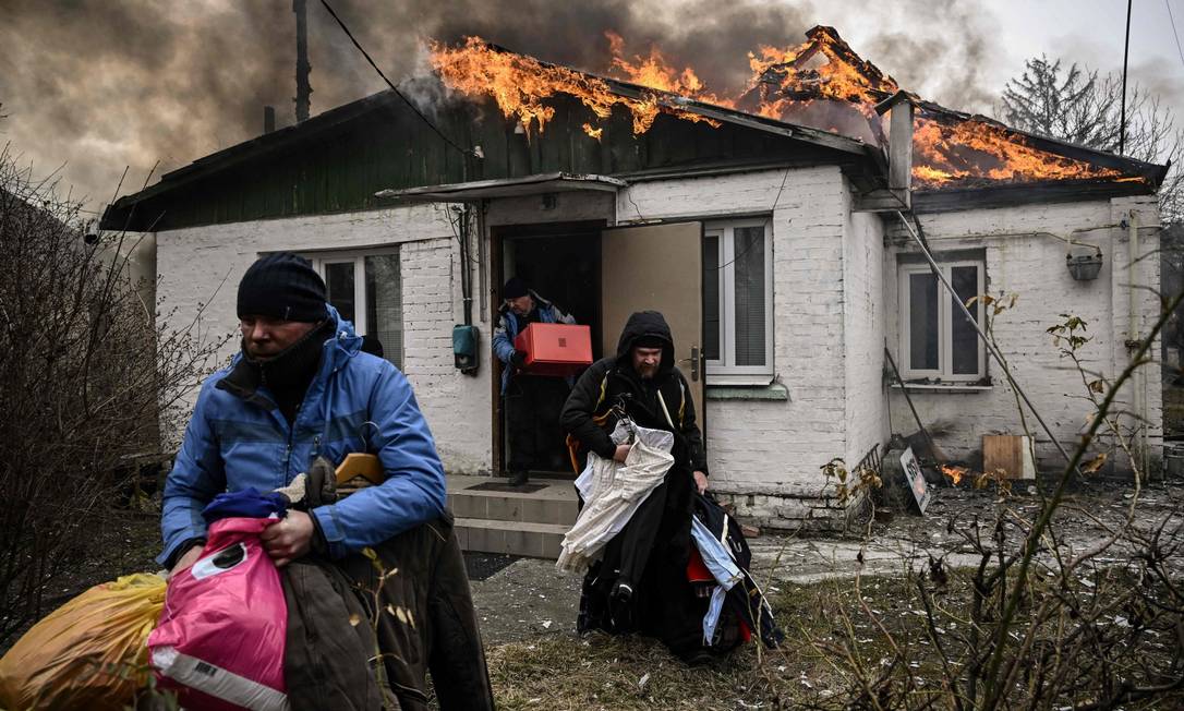 Pessoas removem pertences pessoais de uma casa em chamas após serem bombardeadas na cidade de Irpin Foto: ARIS MESSINIS / AFP