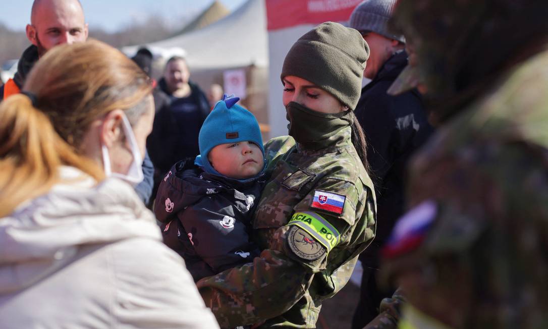 Policial segura um bebê enquanto refugiados da guerra chegam a uma passagem de fronteira em Vysne Nemecke, Eslováquia Foto: LUKASZ GLOWALA / REUTERS
